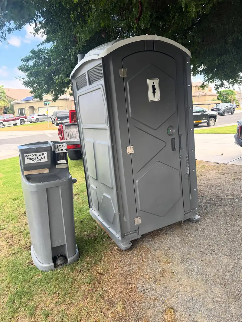 Freestanding hand wash station set next to a gray porta potty on grass