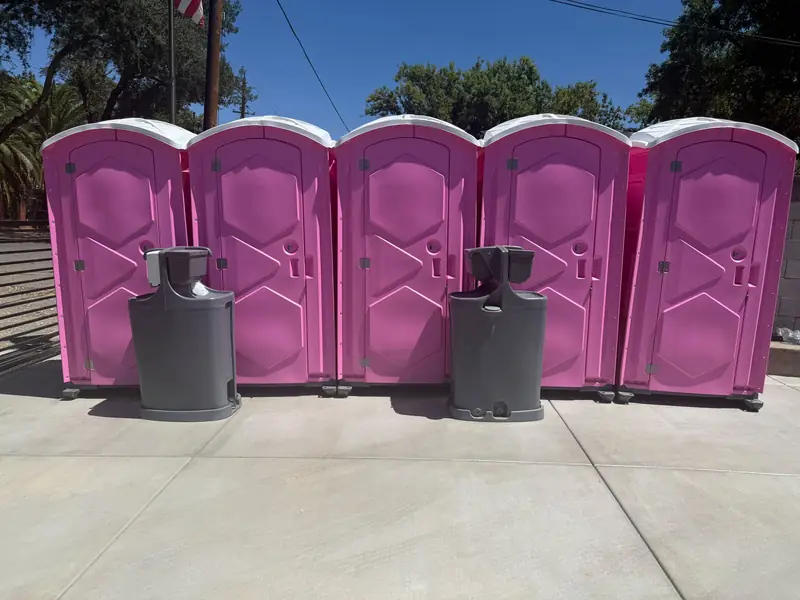 Row of five pink event porta potties with two freestanding hand wash stations on a concrete pad