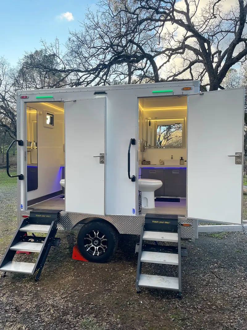 Restroom trailer with open doors and lit vanities set up outdoors