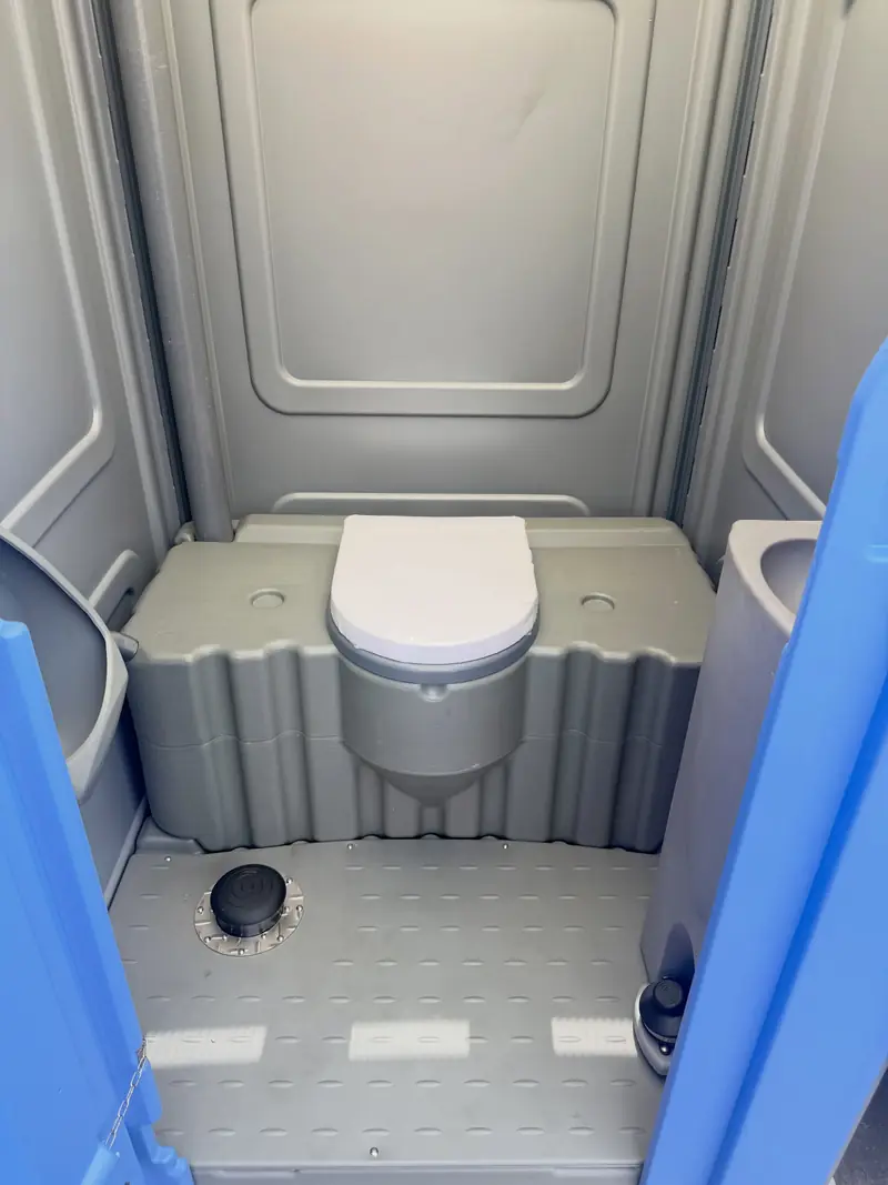 Inside a standard porta potty showing the toilet seat, vent and textured non-slip floor